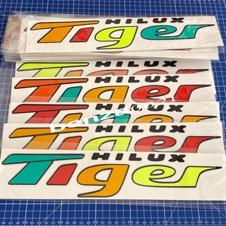 สติ๊กเกอร์* คำว่า TIGER เป็นงานตัดคอมสลับสีๆสะท้อนแสง ติดข้างท้ายกระบะ TOYOTA ขนาด* 6.7 x 34 cm ราคาต่อชุด มี 2 ข้าง